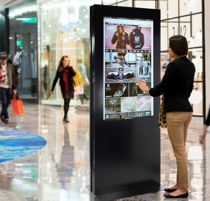 Utente che interagisce con totem touch screen LCD in centro commerciale